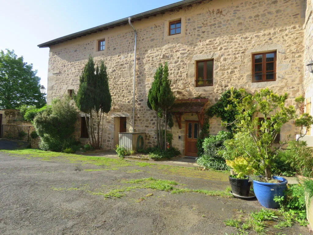Gîte de groupe Les Gîtes du Chastel - Le Livradois à Saint-Bonnet-le-Chastel — Façade en pierre du gîte du Chastel avec jardin planté de cyprès et entrée voûtée, capacité 15 personnes