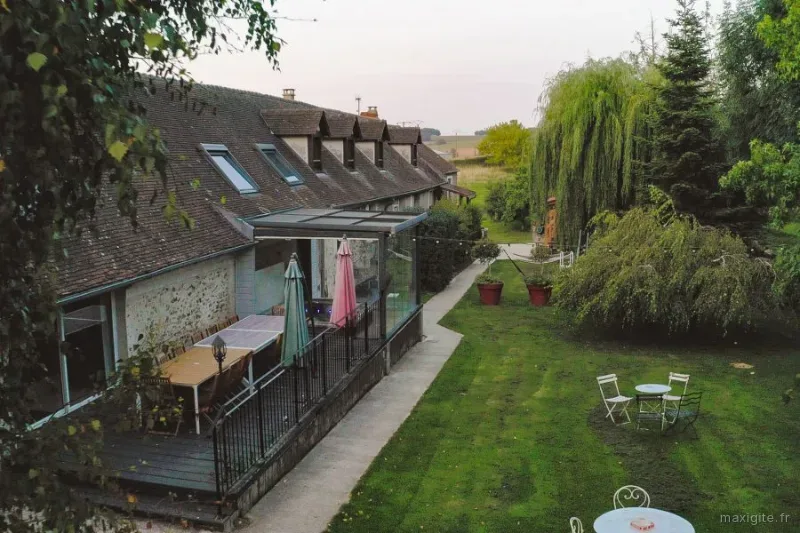 Vue aérienne de la ferme en pierre avec terrasse couverte, jardin arboré et grands saules pleureurs