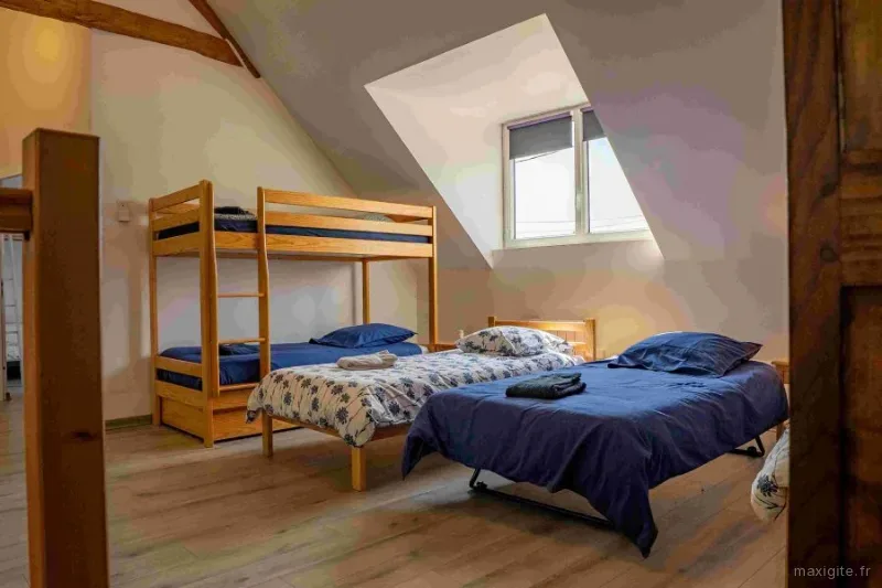 Chambre mansardée avec lit double, lits superposés en bois et velux sous charpente