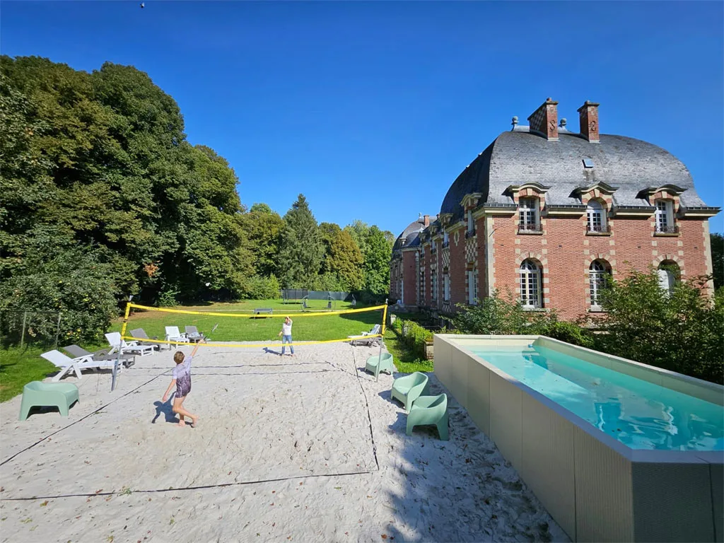 Gîte de groupe Château de Goyencourt à Goyencourt — Façade en briques roses du château vue depuis le jardin, avec piscine hors-sol et espace beach-volley, capacité 60 personnes