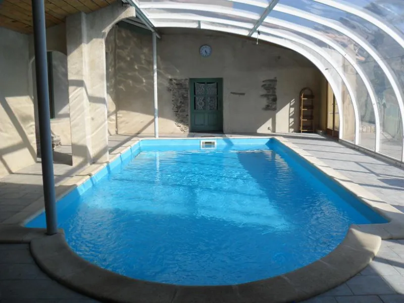 Piscine couverte chauffée avec structure vitrée, entourée de murs en pierre