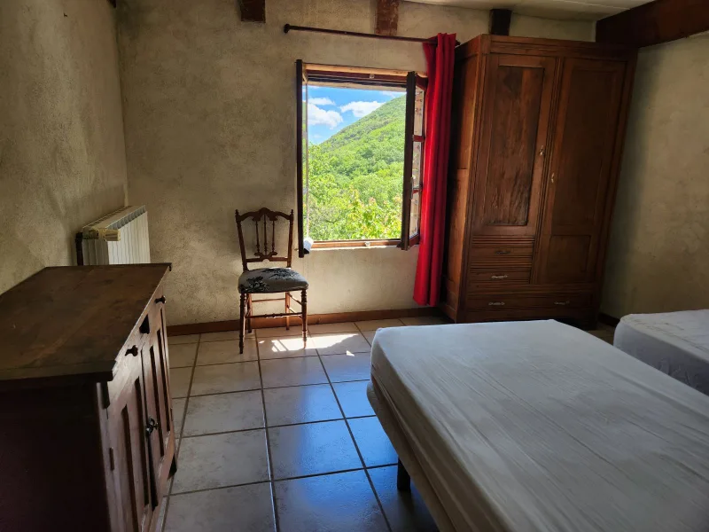 Chambre sous poutres apparentes avec armoire ancienne et vue sur la vallée verdoyante