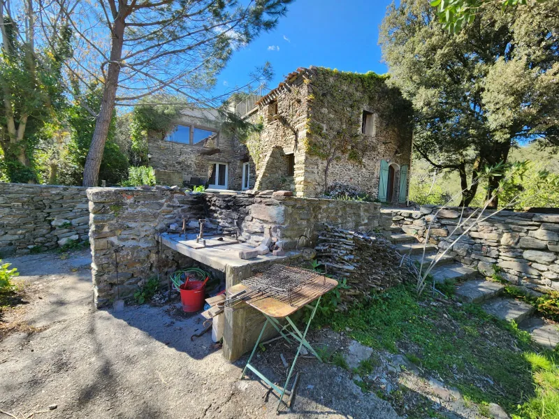 Coin barbecue en pierre sous la façade du gîte, avec vue sur les collines boisées