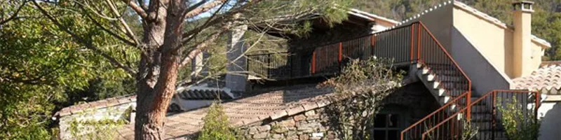Gîte de groupe Grand Gîte des Jourdets à Lairière — Façade en pierre du gîte entourée de pins et d'oliviers, sous un grand ciel bleu, capacité 30 personnes