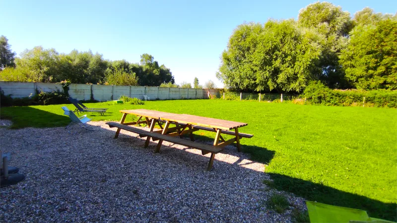 Table de pique-nique en bois posée sur l'allée de gravier, entourée d'une grande pelouse