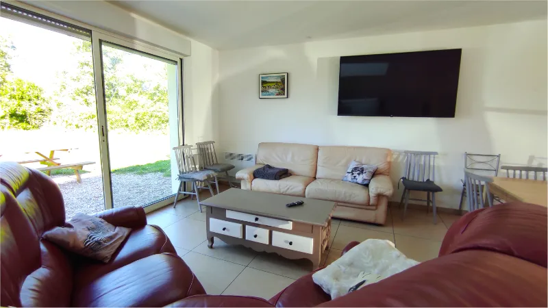 Salon avec canapés en cuir et grand écran, ouvert sur la terrasse par une baie vitrée