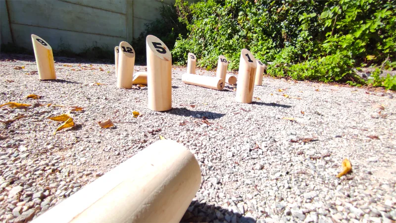Jeu de mölkky installé sur l'allée de gravier, au bord de la pelouse et des haies