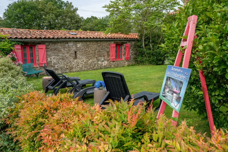 Façade en pierre du gîte avec volets rouges, entourée d'un jardin fleuri et arboré