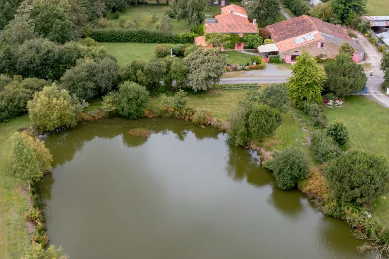 Vue aérienne du gîte au bord de l'étang privé, entouré de prairies et de haies bocagères