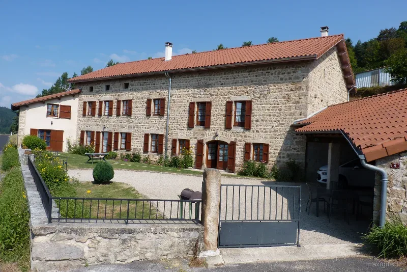 Façade en pierre du gîte Les Bruyères avec jardin verdoyant et ciel dégagé sur le plateau