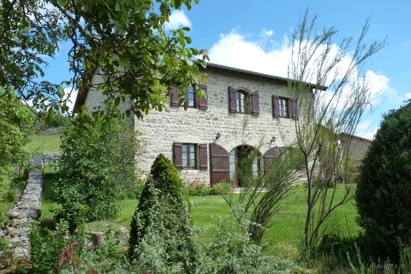 Façade en pierre du gîte Les Lilas couverte de lierre, entourée d'un jardin arboré