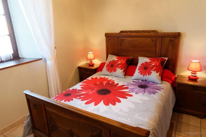 Chambre avec lit double, tête de lit en bois sculpté et parure fleurie rouge