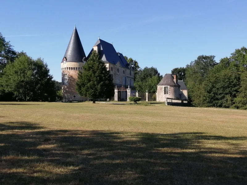 Château du XVe siècle avec tourelle conique, entouré de grands arbres et d'une pelouse dégagée