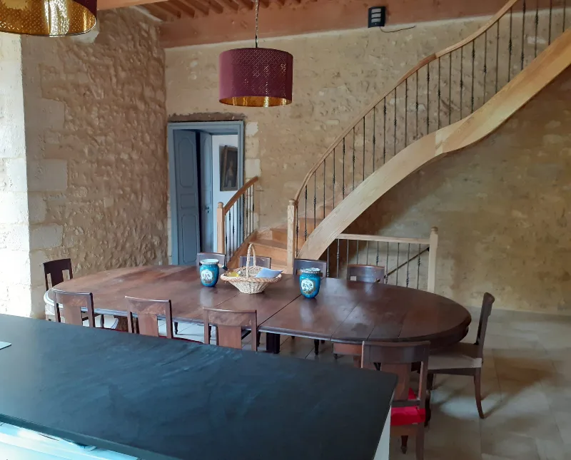 Salle avec grande table ronde en bois et escalier en bois menant à l'étage