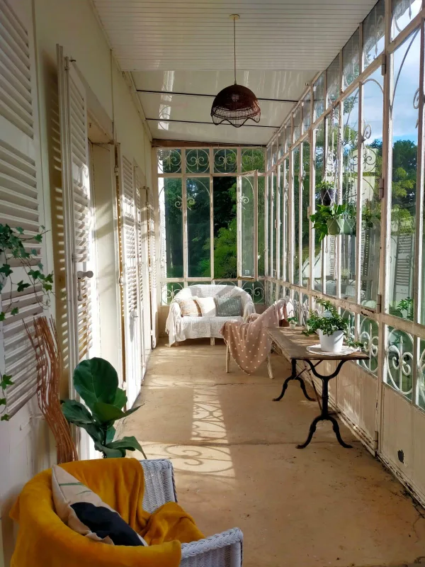 Véranda lumineuse avec verrière ancienne, fauteuils en osier et plantes vertes