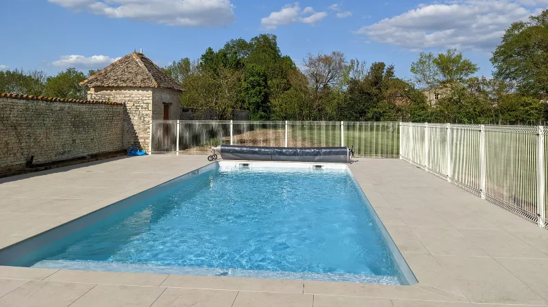 Piscine privée chauffée entourée de dallage clair, avec pigeonnier en pierre et grand jardin en arrière-plan