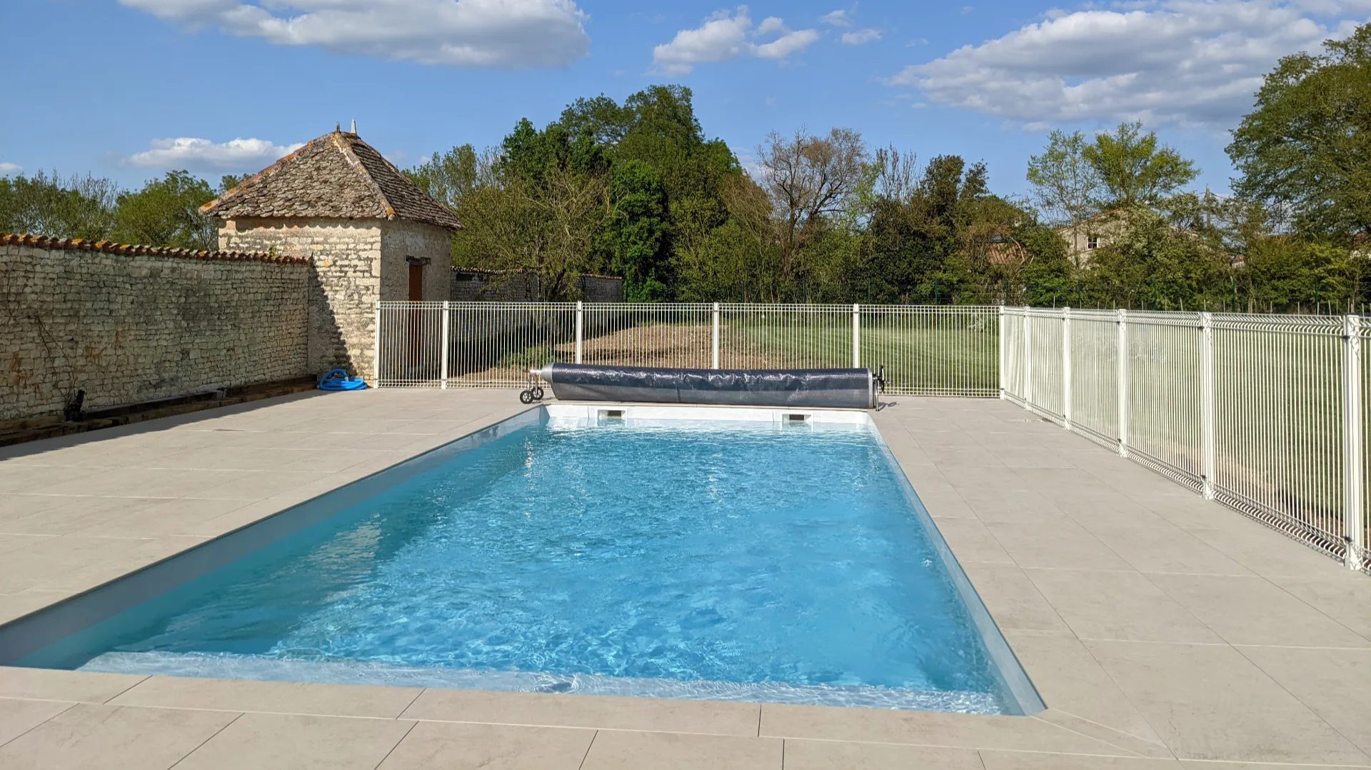 Gîte de groupe Le Fournil - Gîtes Les Grandes Chaumes à Surgères — Piscine privée chauffée entourée de dallage clair, avec pigeonnier en pierre et grand jardin en arrière-plan, capacité 12 personnes