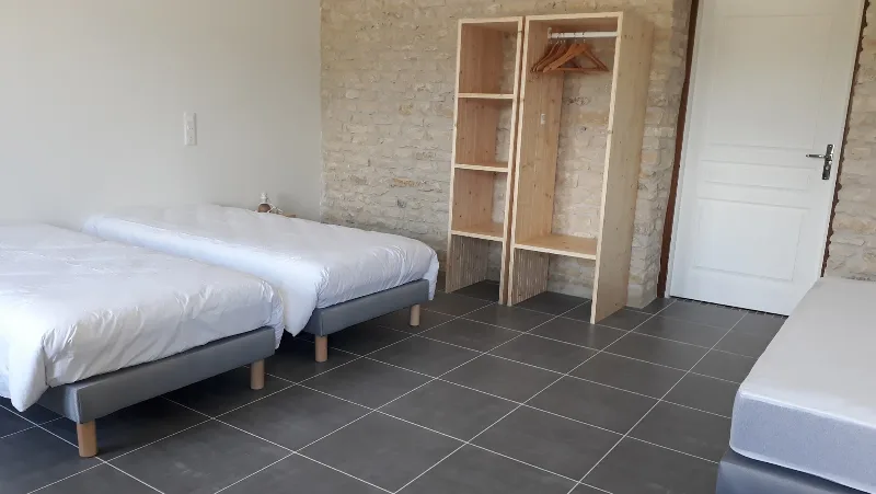 Chambre avec deux lits doubles, mur en pierre apparente et dressing en bois clair ouvert