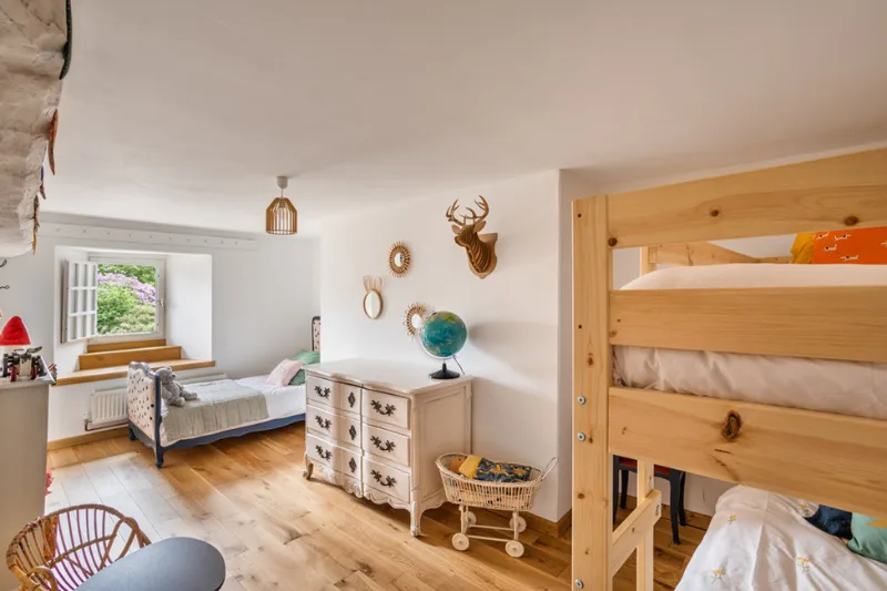 Chambre enfants avec lits superposés en bois clair, lit simple et vue sur le jardin