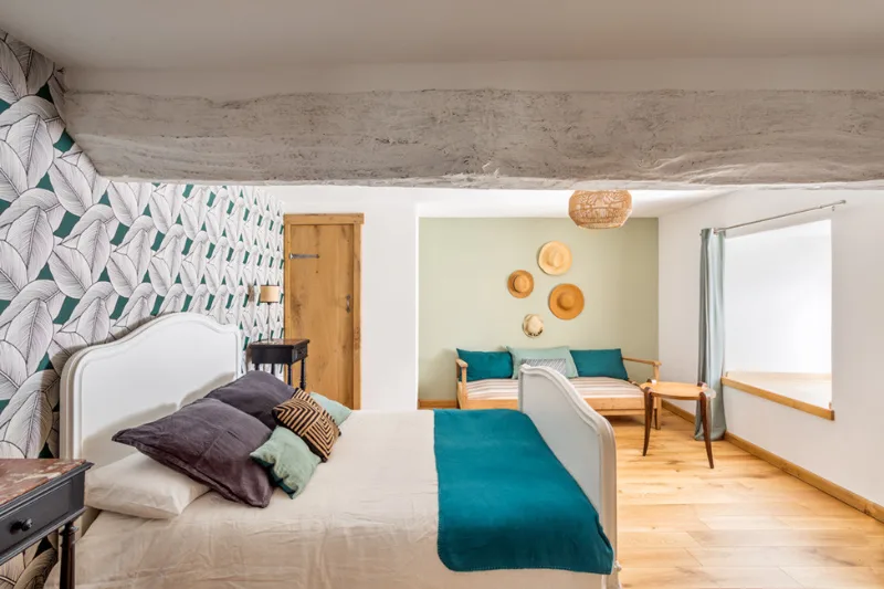 Chambre double avec tête de lit blanche, coin salon attenant et papier peint feuillage