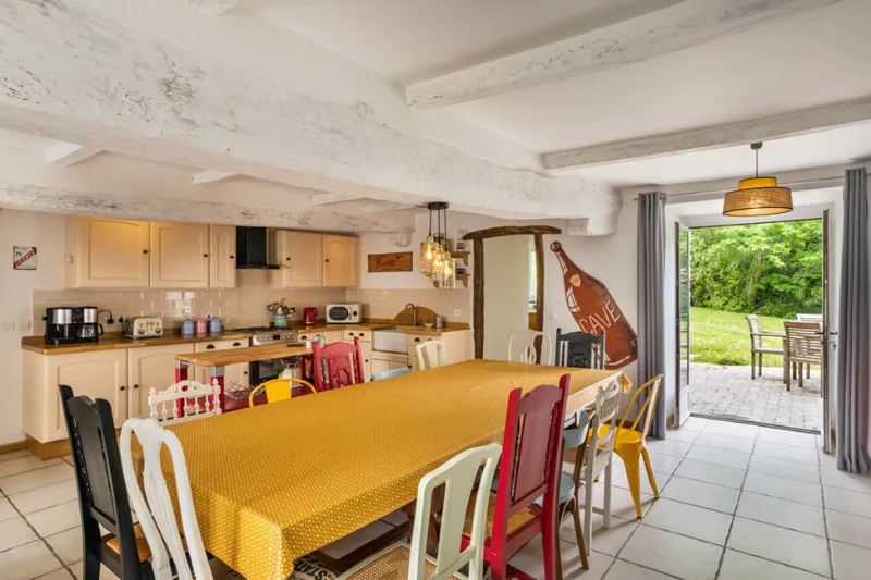 Cuisine-salle à manger avec grande tablée dressée, mobilier coloré et porte ouverte sur la terrasse