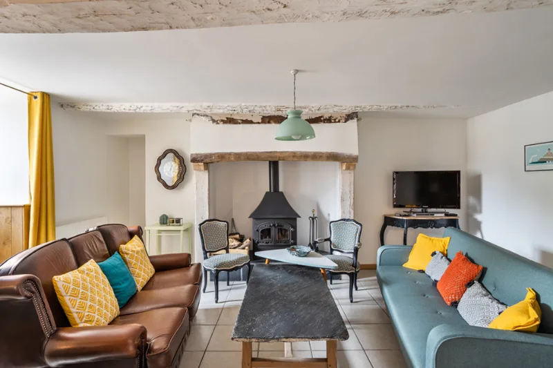 Salon cosy avec poêle à bois, poutres apaisantes et canapés colorés autour d'une table basse en ardoise