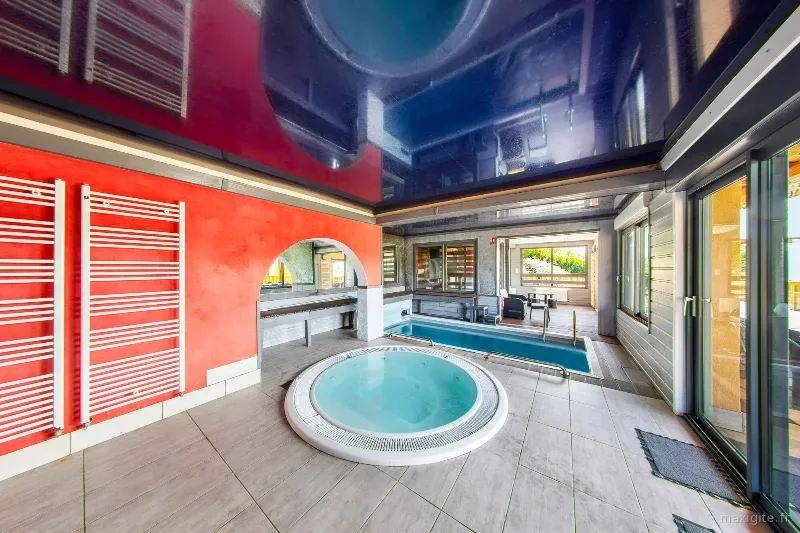 Piscine couverte et spa jacuzzi aux reflets rouge et bleu, espace bien-être privatif