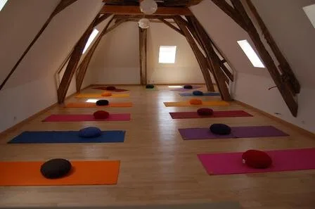 Salle d'activité sous charpente en bois apparente, aménagée en espace de yoga et méditation