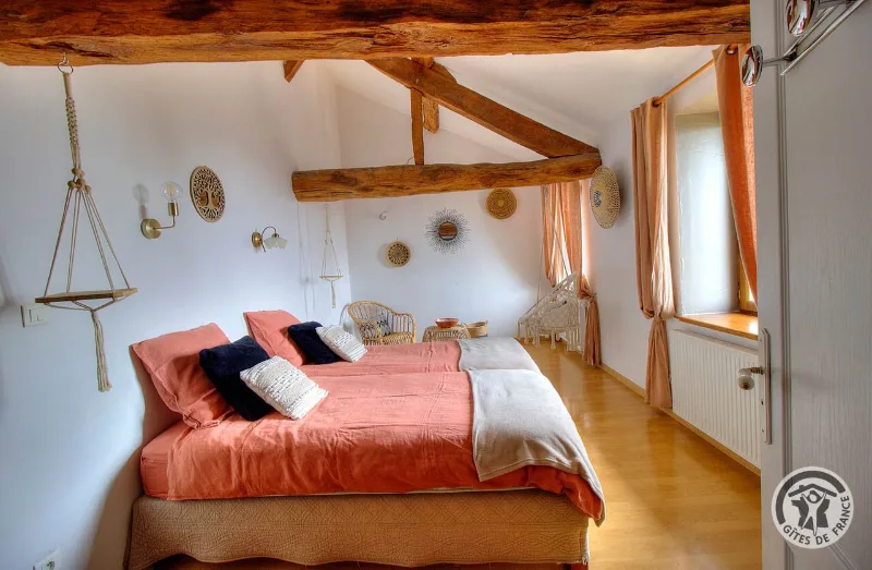 Chambre sous charpente en bois apparente, lit double aux teintes corail et coin lecture