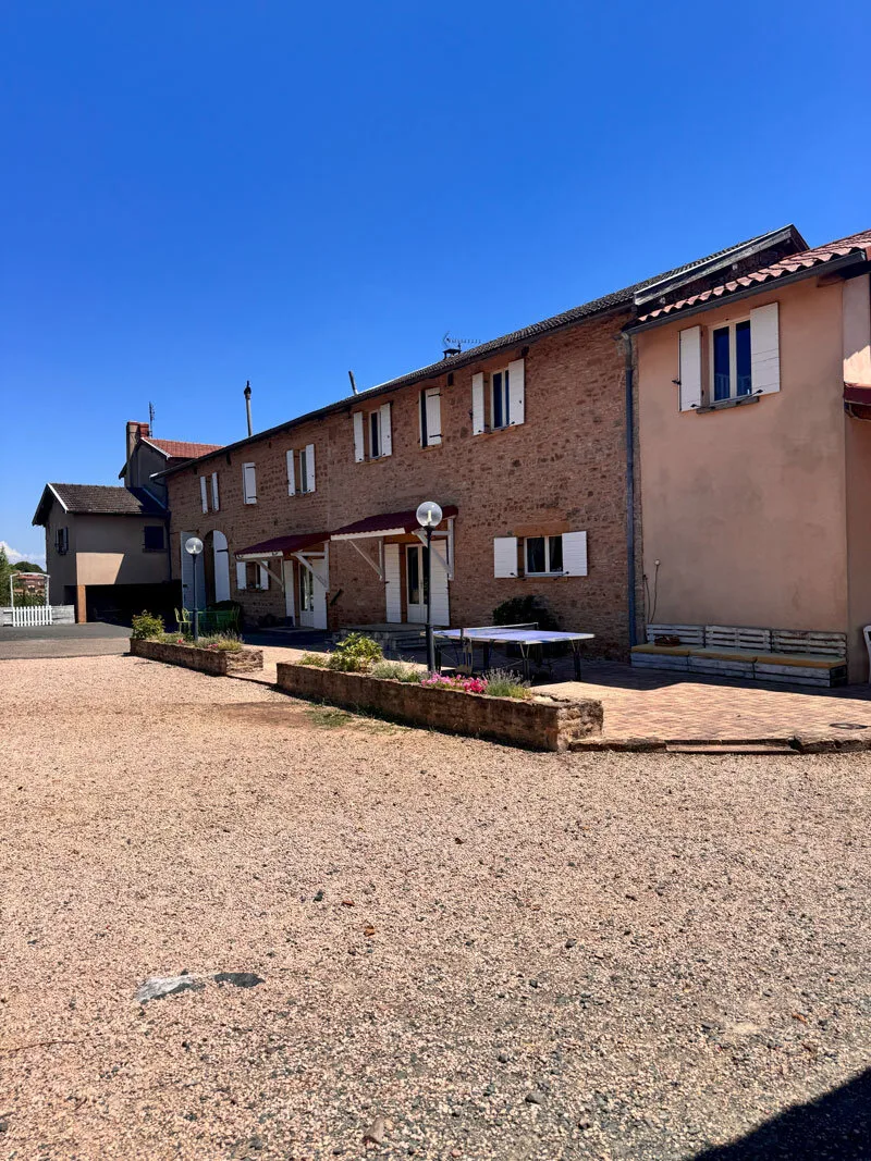 Gîte de groupe Domaine des Vignes d'Hôtes à Bagnols — Façade en pierre dorée typique du Beaujolais, longue bâtisse sous ciel bleu avec volets blancs, capacité 30 personnes