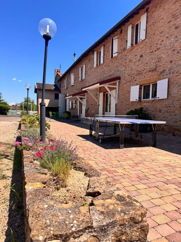 Façade en pierre dorée avec allée pavée, réverbères et table de ping-pong extérieure