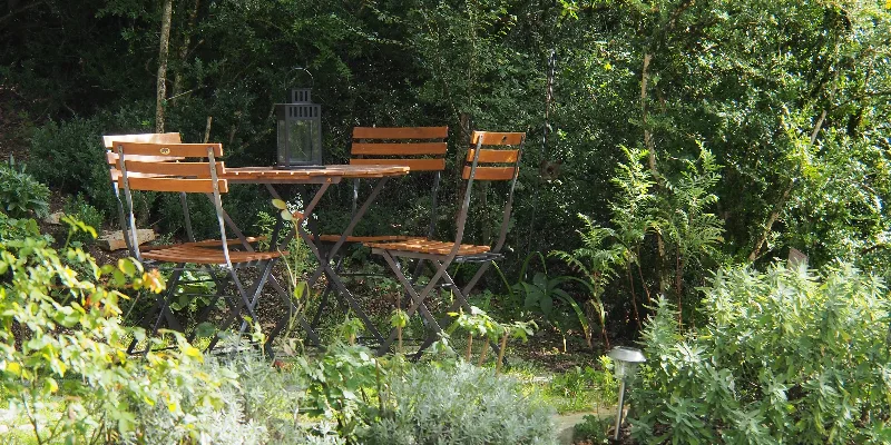 Coin salon de jardin ombragé avec table ronde et lanterne, entouré de verdure