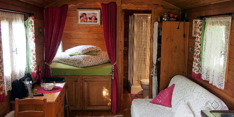 Intérieur cosy de la roulotte avec lit surélevé, rideaux rouges et salle d'eau attenante