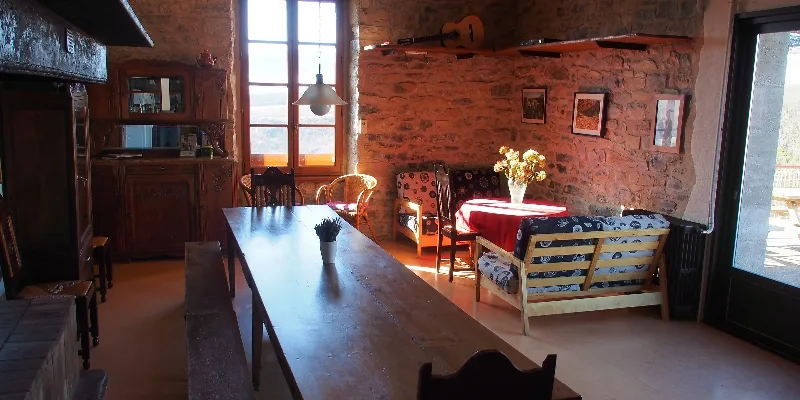 Grande salle à vivre en pierre avec longue table en bois, cheminée et coin salon