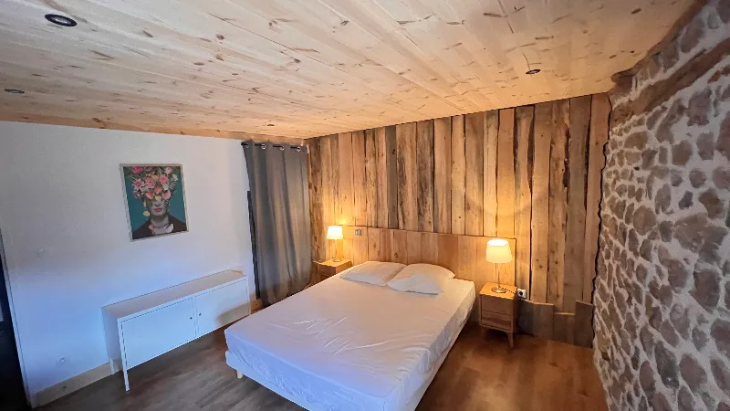 Chambre avec mur en pierre apparente, lit double et éclairage tamisé
