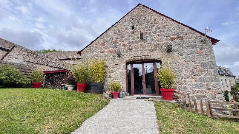 Façade en pierre vue de trois-quarts avec porte-fenêtre et jardin engazonné