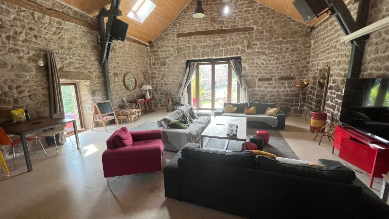 Salon avec canapés et baie vitrée donnant sur l'extérieur, sous charpente en pierre et bois
