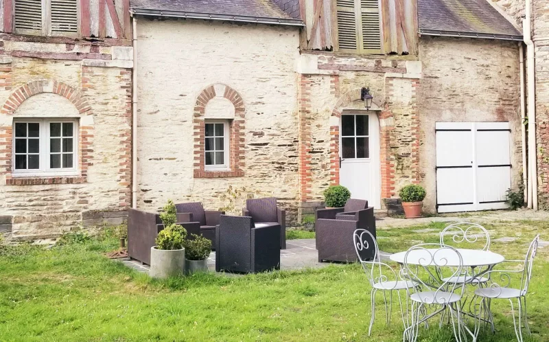 Façade de la longère en pierre du gîte avec fenêtres en briques et salon de jardin en osier