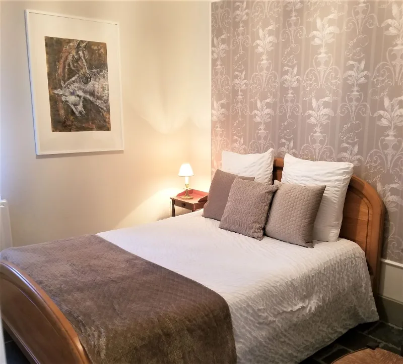 Chambre avec lit en bois, tête de lit capitonnée et papier peint à motifs floraux