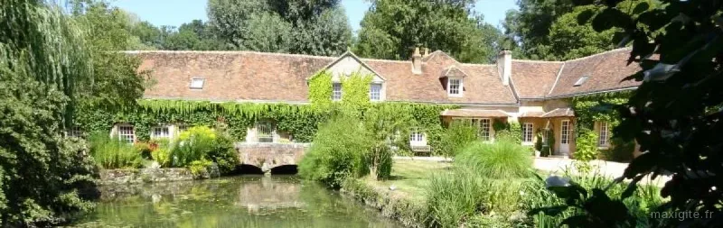 Longère couverte de vigne vierge reflétée dans l'étang du moulin, avec petit pont de pierre
