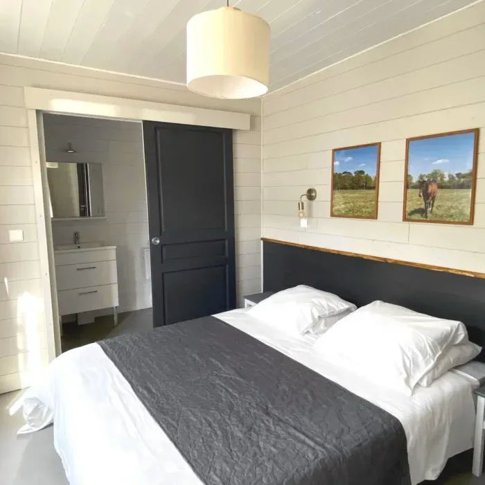 Chambre double avec tête de lit foncée, linge blanc et salle d'eau attenante