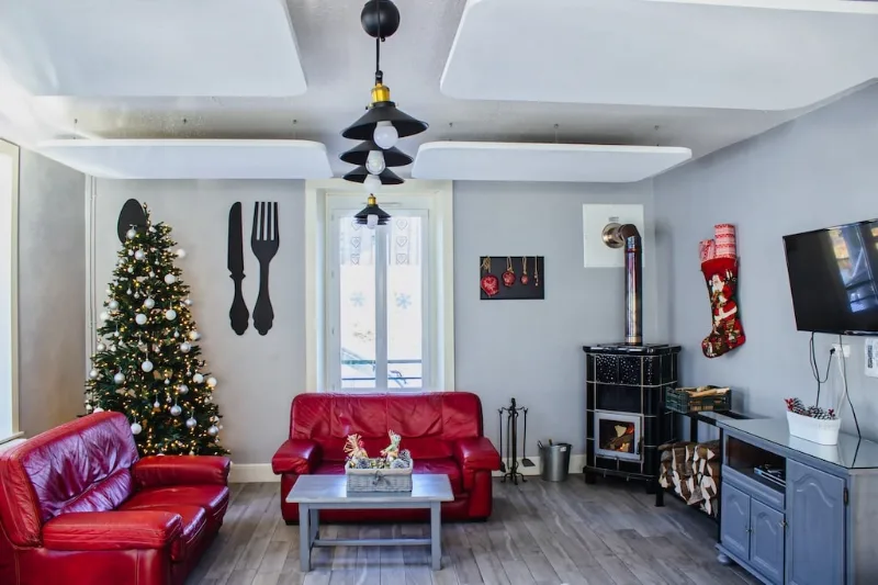 Salon cosy avec canapés en cuir rouge, poêle à bois et sapin de Noël
