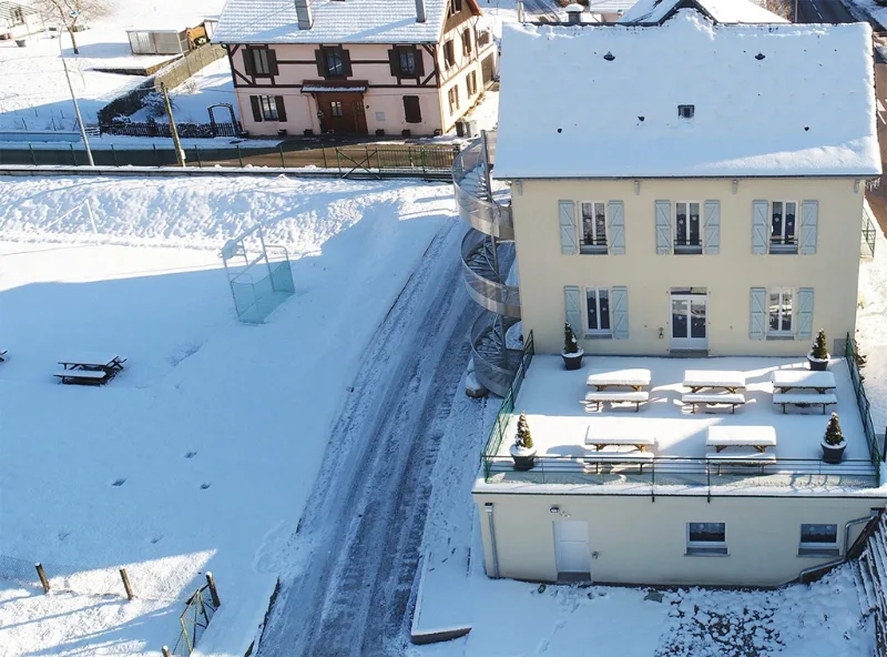 Terrasse extérieure enneigée avec tables de pique-nique face à la vallée