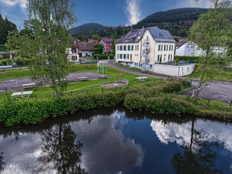 Vue aérienne de la maison vosgienne au bord d'un étang, entourée de collines boisées
