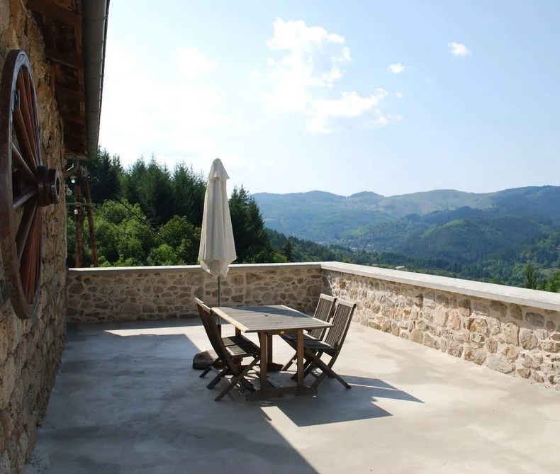 Grande terrasse en pierre avec table et vue panoramique à 180° sur les montagnes ardéchoises