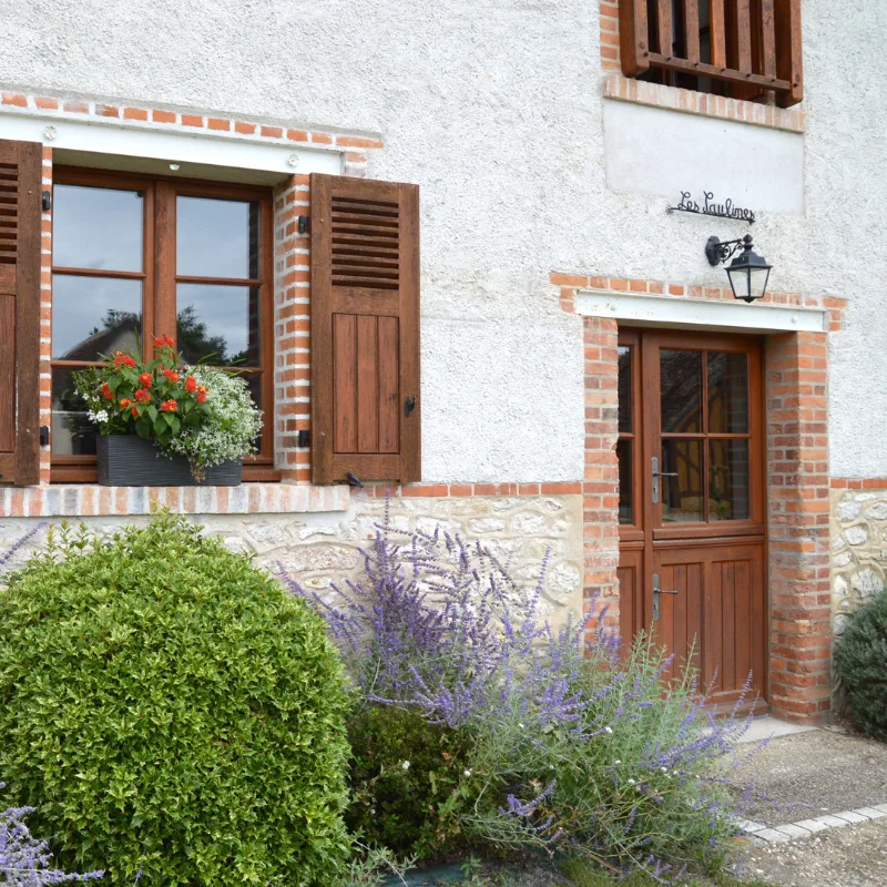 Façade fleurie du gîte Les Saulines avec volets bois et briques