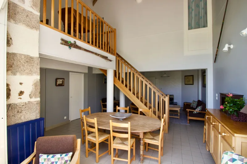 Salle à manger commune sous la mezzanine avec grande table ronde en bois