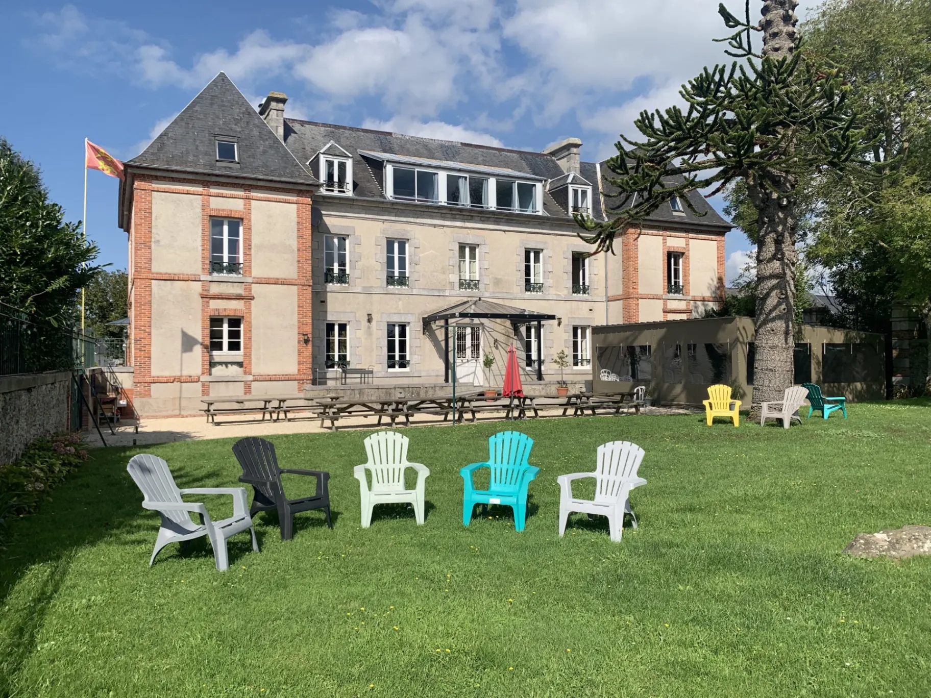 Gîte de groupe Château des Forges à Gouville-sur-Mer — Façade du château des Forges en pierre avec grand jardin arboré et pelouse, capacité 53 personnes