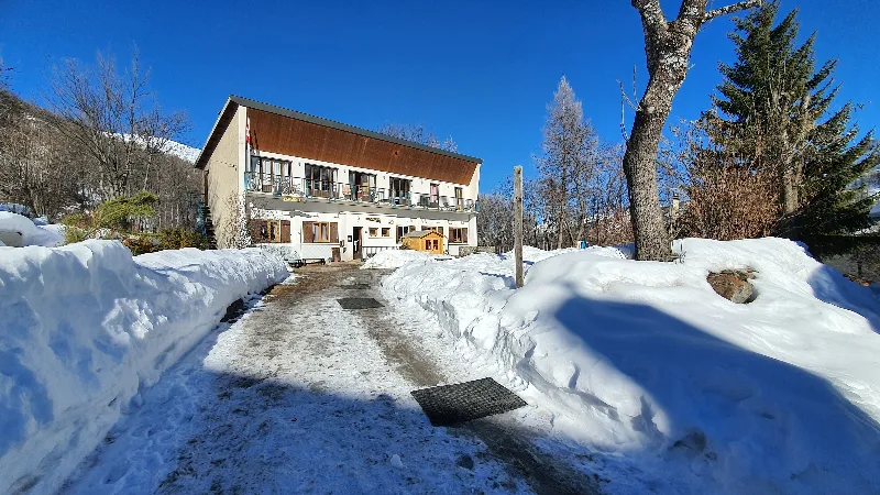 Chemin d'accès déneigé menant à l'entrée du gîte, façade et balcons visibles
