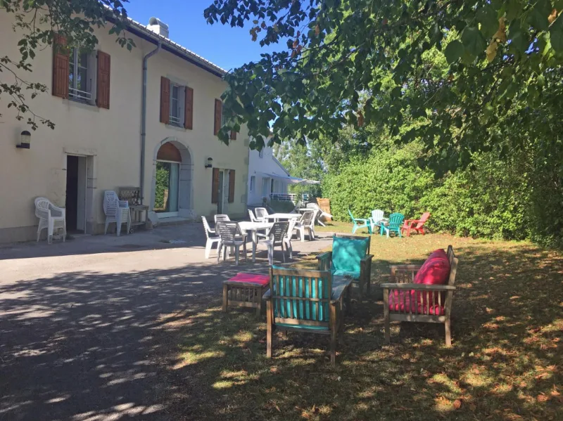 Terrasse extérieure ombragée avec tables, chaises et salon de jardin coloré devant le bâtiment